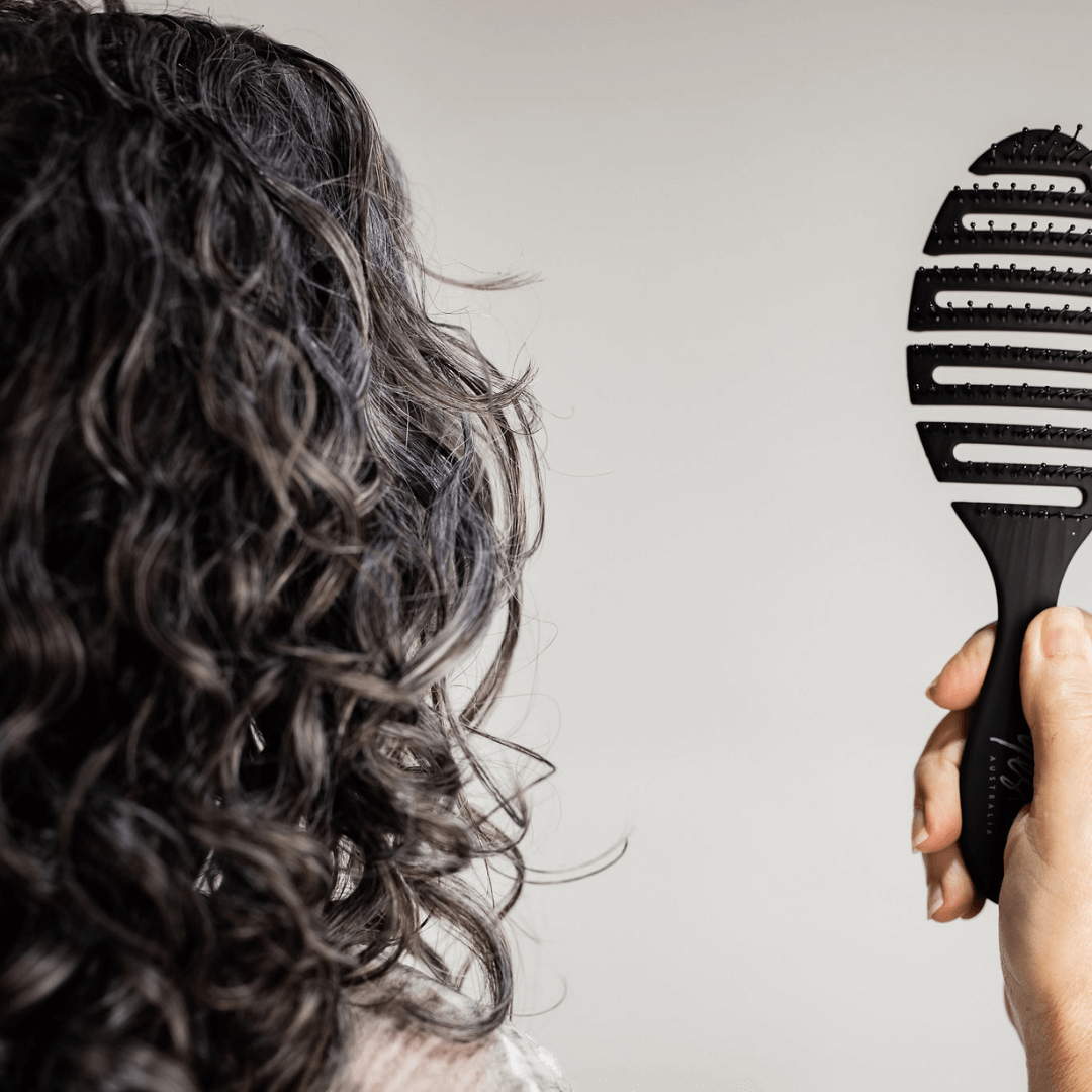 brush being held next to curly haired woman